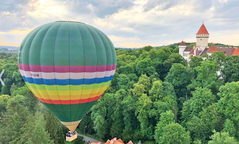 彩虹彩色热气球横跨森林低层穿过城堡